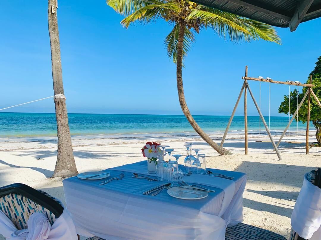 Una mesa frente a la playa, dispuesta para la cena y con un jarrón de flores, con vista al océano.