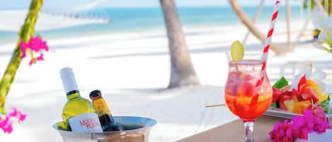 Una mesa frente al mar, con una bebida, una botella de vino y un plato de fruta.