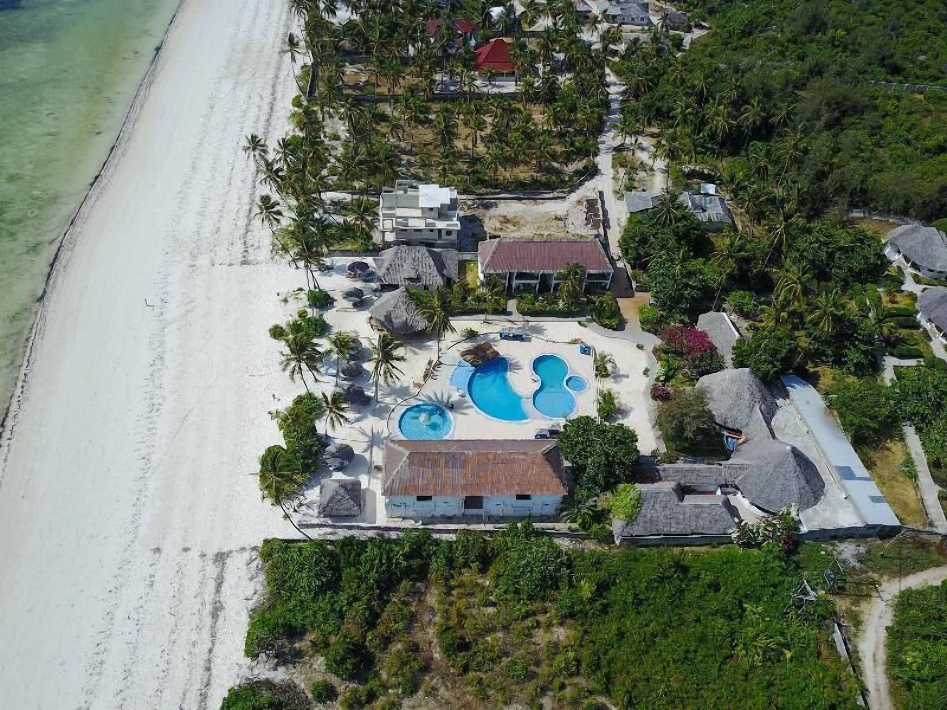 An aerial view of a resort with a large swimming pool, beachfront properties, and lush vegetation.