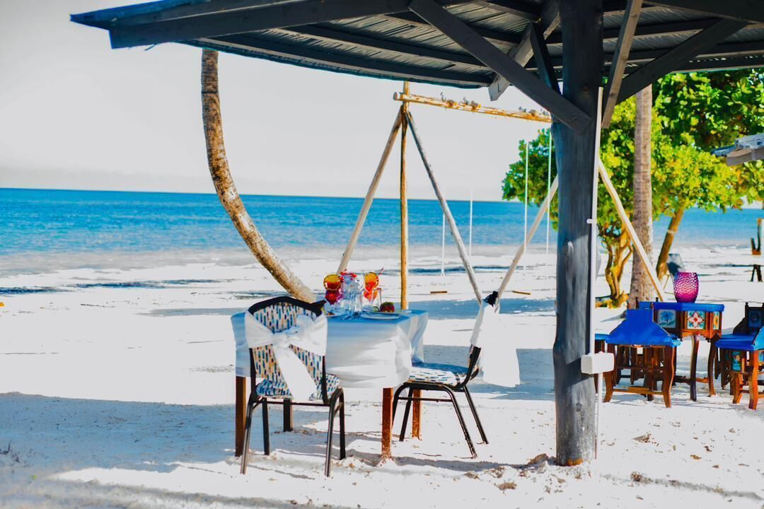 Ein Essbereich direkt am Strand mit Tisch und Stühlen unter einer Holzkonstruktion, mit Blick aufs Meer.