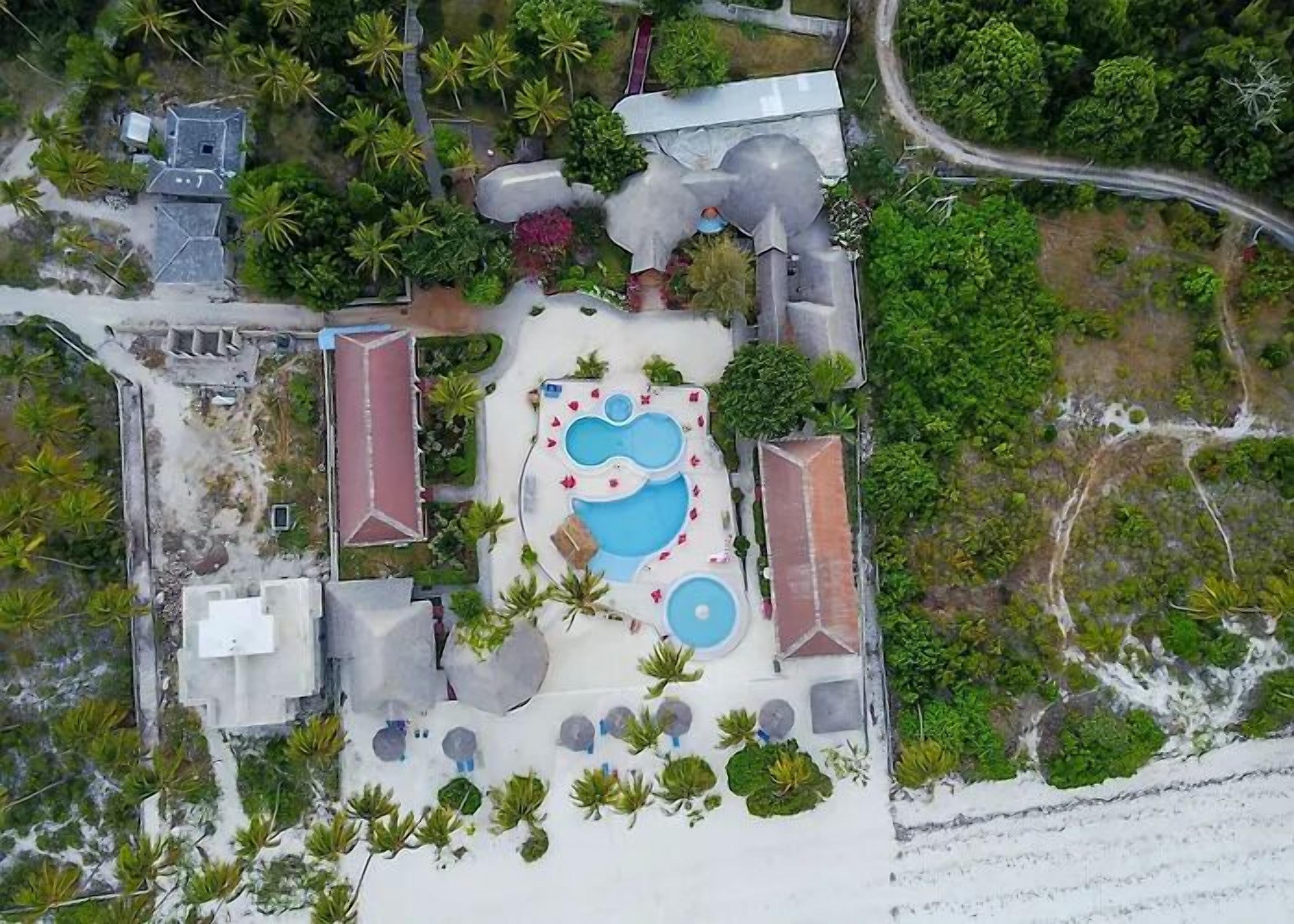 Luchtbeeld van een resort met meerdere zwembaden, palmbomen en een strand.
