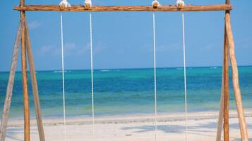 A wooden swing set on a sandy beach with clear blue water in the background.