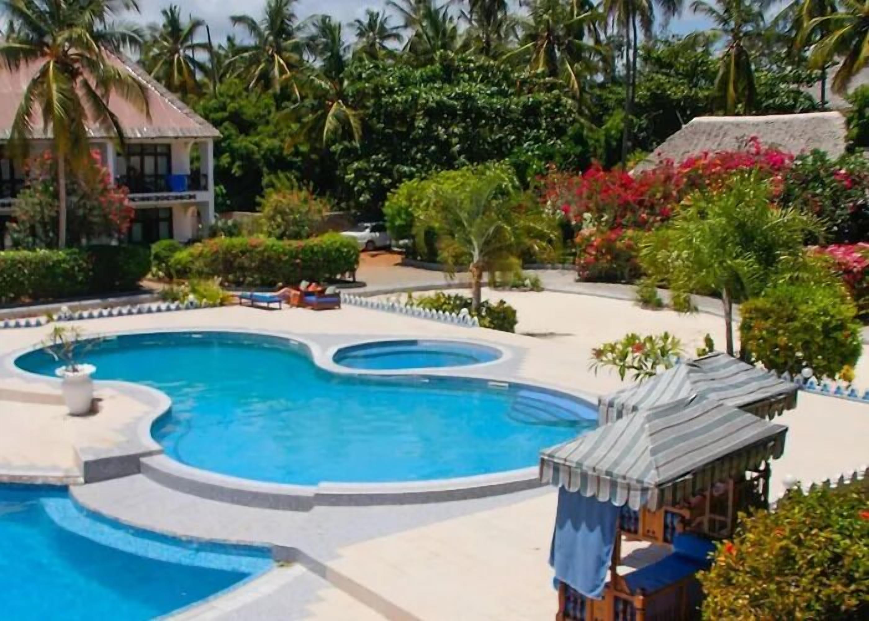 A resort with a large, curved swimming pool surrounded by lush greenery and palm trees.