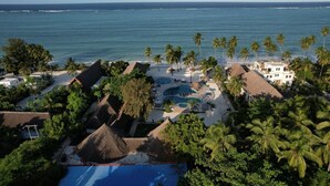 A resort with a pool area, palm trees, and a view of the ocean. - Protels La Plage (Bwejuu)