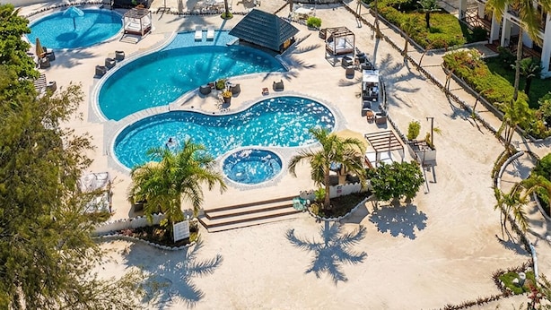 A resort with a large, multi-tiered swimming pool surrounded by palm trees and beach chairs. - Protels La Plage (Bwejuu)