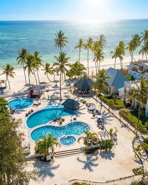 Un complexe hôtelier doté d’une grande piscine à plusieurs niveaux, entourée de palmiers et de chaises de plage.