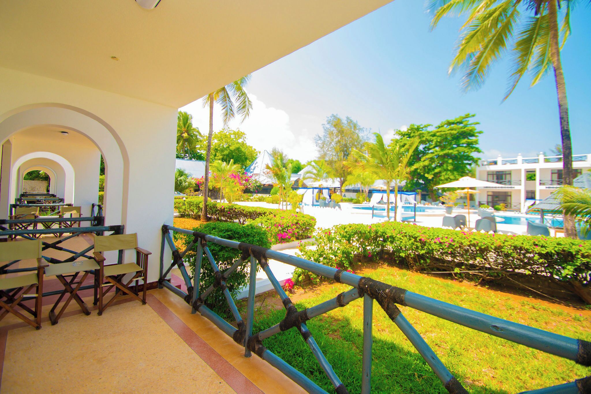 A covered outdoor area with a pool, palm trees, and a seating area with tables and chairs.