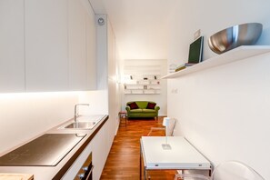 A modern kitchen with a built-in stove, a dining area with a table and chairs, and a green sofa in the background.