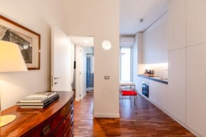 Une cuisine moderne avec des meubles blancs, un coin repas agrĂ©mentĂ© dâune chaise rouge et un couloir menant Ă une autre piĂšce.