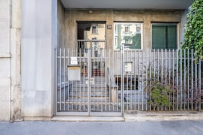 A gated entrance with a metal fence, a set of stairs leading to a door, and a building facade with a number '29' visible.