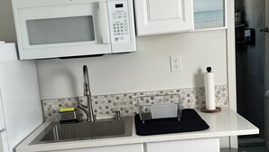 A modern kitchen with white cabinetry, a stainless steel sink, and a microwave. - Cozy studio in a great location! (Largo)