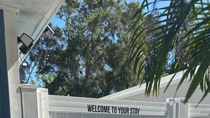 A white fence with the text "WELCOME TO YOUR STAY" and a well-maintained lawn. - Cozy studio in a great location! (Largo)