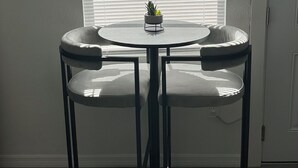 A round table with two chairs, a potted plant on the table, and a window with blinds in the background. - Cozy studio in a great location! (Largo)