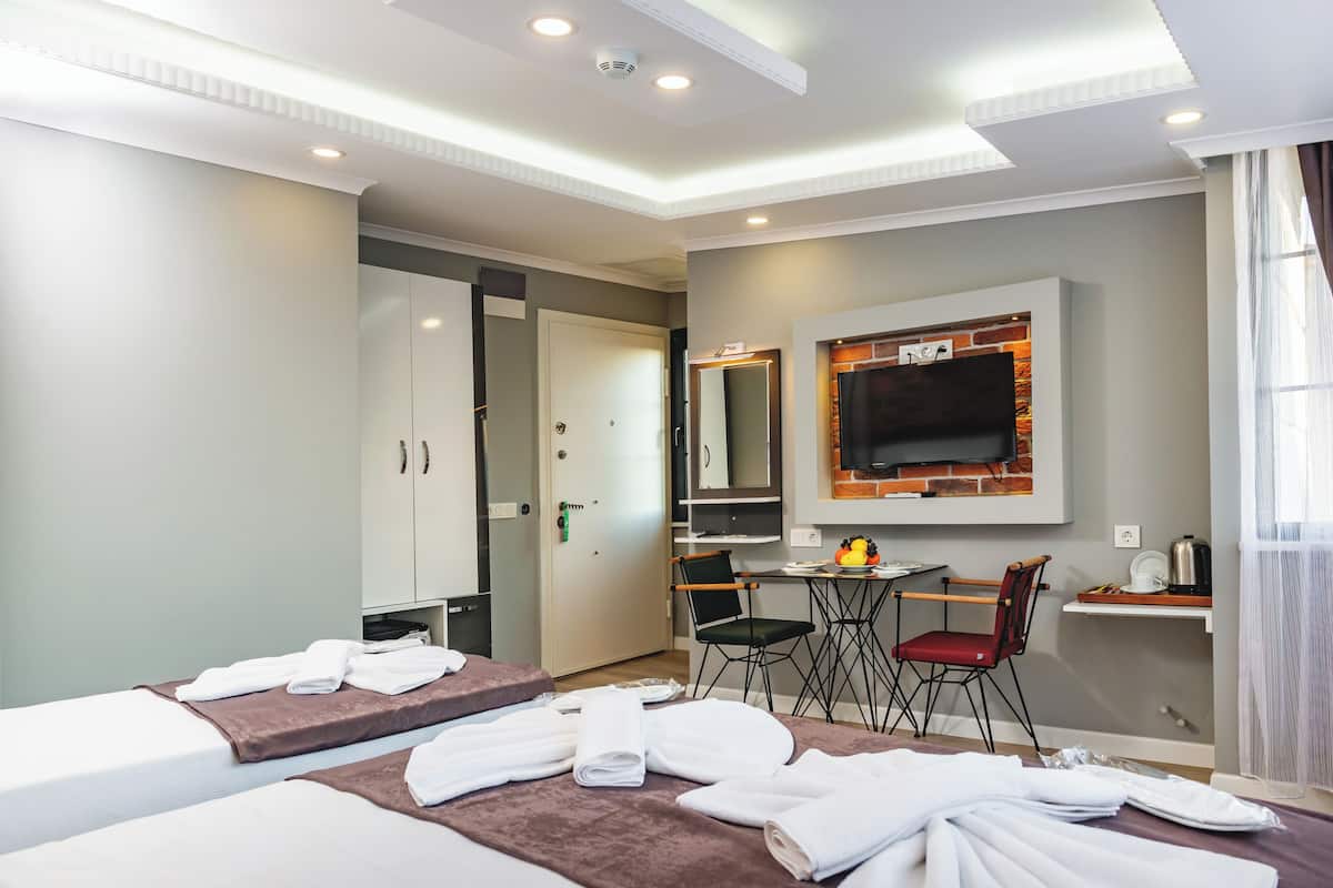 A hotel room with two beds, a desk with chairs, a TV, and a bathroom.