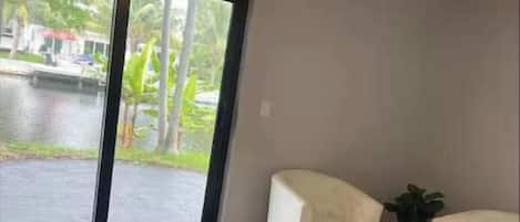 Un dormitorio con una cama grande, dos sillones blancos, un ventilador de techo y vistas a un cuerpo de agua a través de una puerta corrediza.