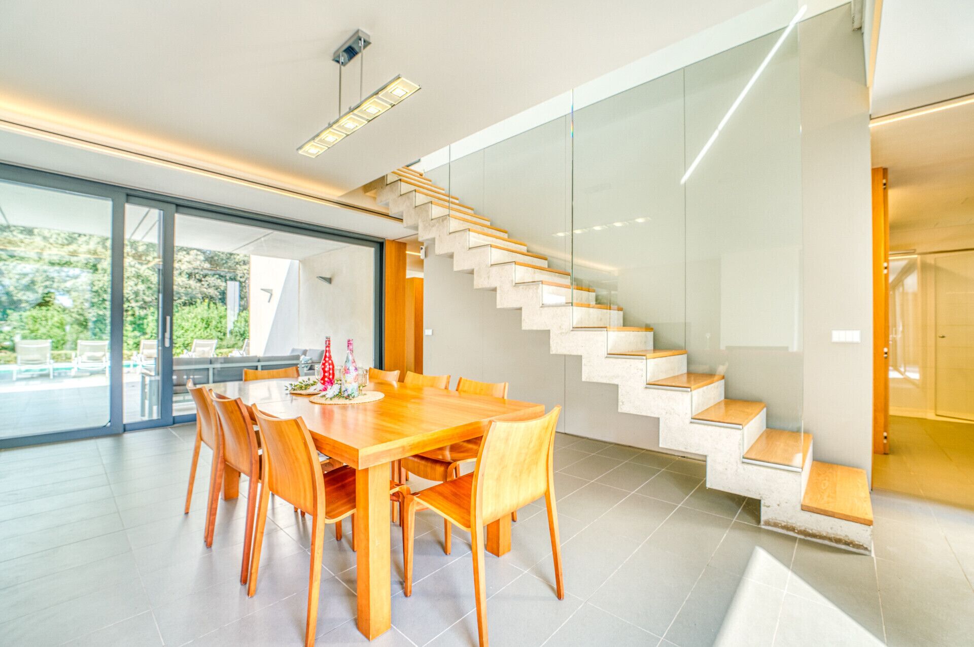 A modern dining area with a wooden table and chairs, a glass staircase, and a view of the outdoors.