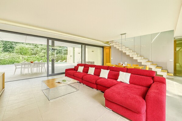 Una sala moderna con un sofá seccional rojo, una escalera de cristal y un comedor con sillas blancas y una mesa.