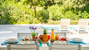 An outdoor dining area with a table set for breakfast, surrounded by chairs, with a pool and greenery in the background. - Villa Alzina house with pool in Majorca (Sa Pobla)