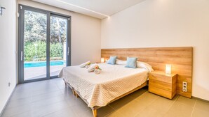 A modern bedroom with a large bed, wooden headboard, and a view of a swimming pool through a sliding glass door. - Villa Alzina house with pool in Majorca (Sa Pobla)