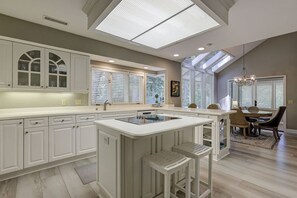 A kitchen with a central island, white cabinetry, and a dining area with a chandelier.