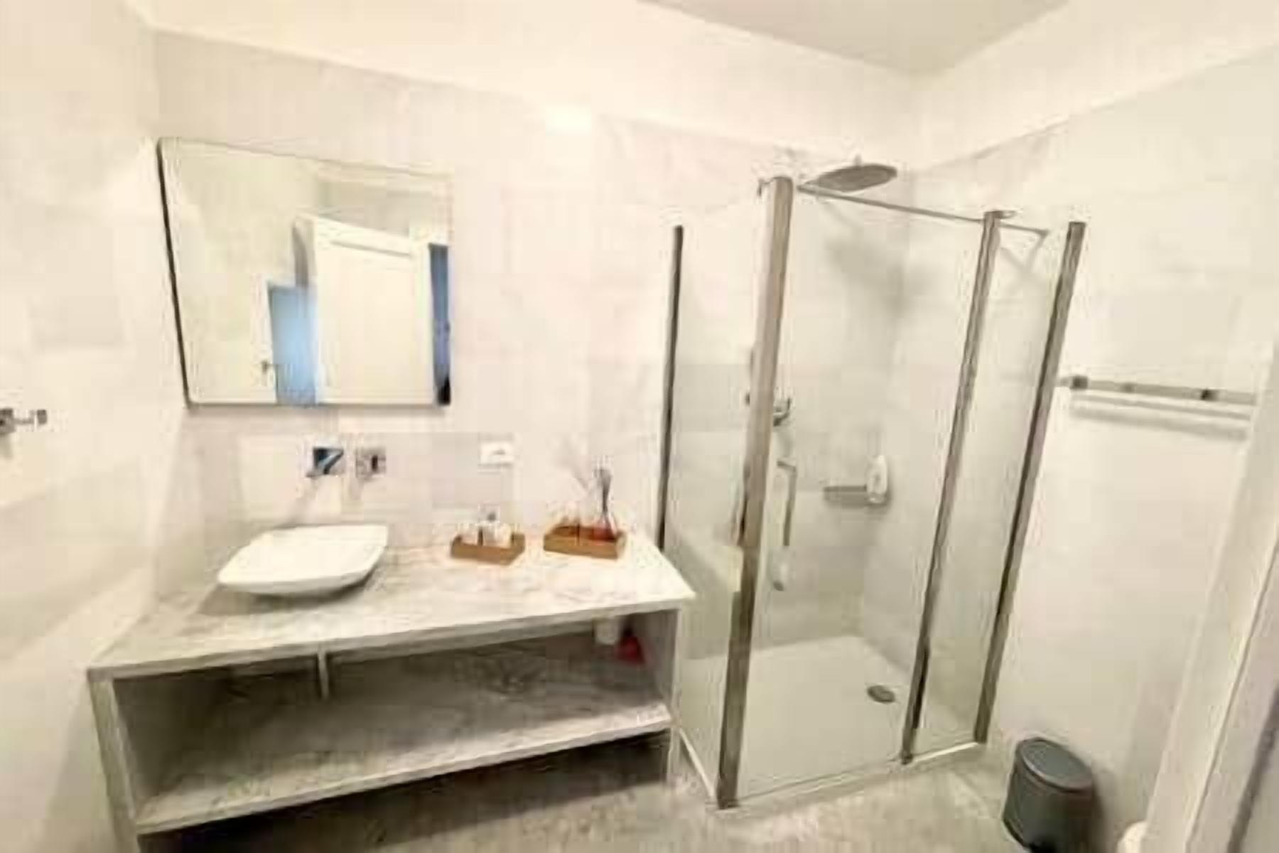 Un baño moderno con cabina de ducha de vidrio, lavamanos de mármol y espejo sobre el mueble.