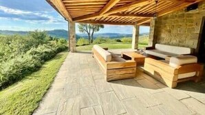 An outdoor patio with wooden furniture, a stone floor, and a view of the landscape. - Luxury Villa Podere Del Grasso, Tuscany, ITALY (Castel del Piano)