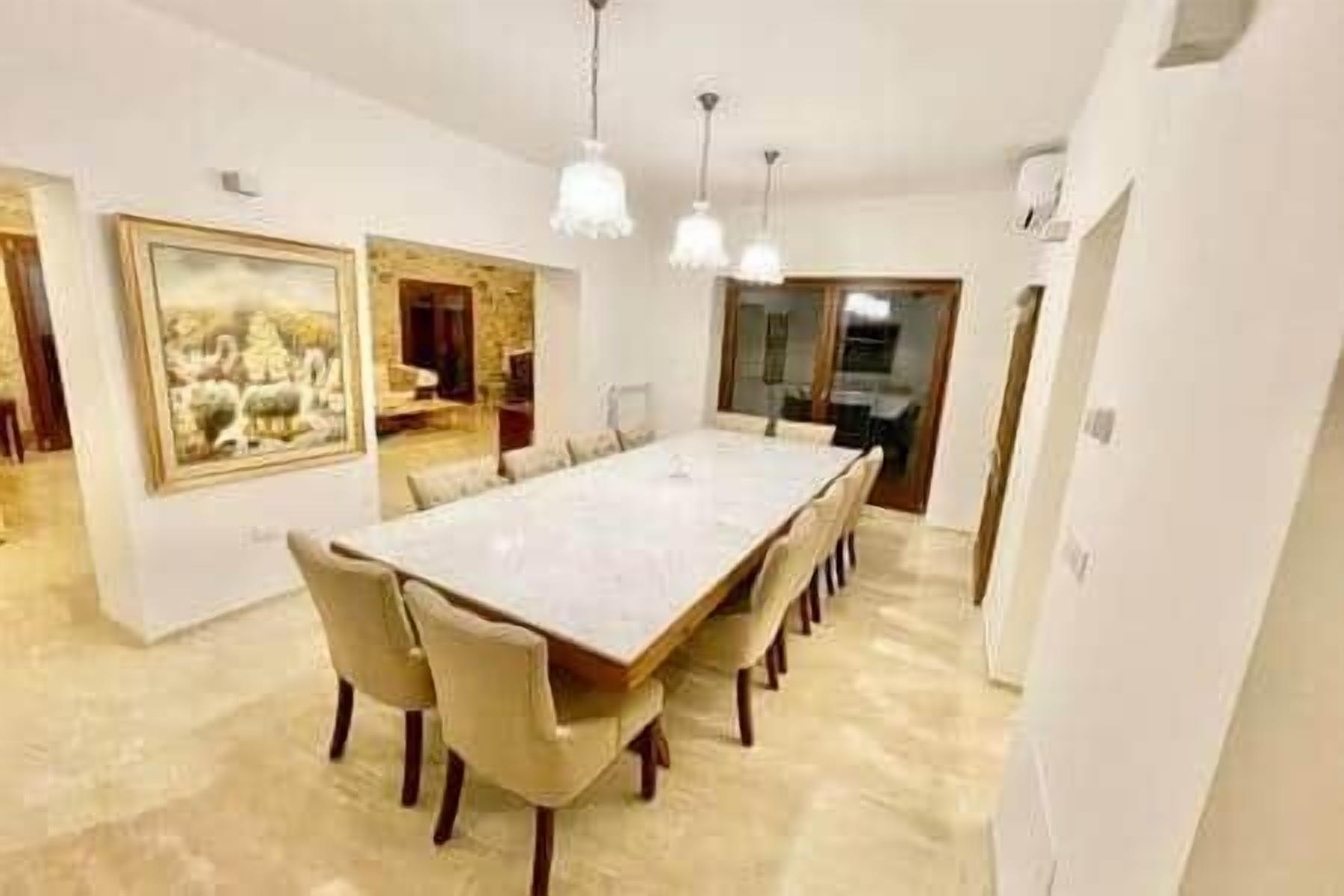 A dining room with a long table, chairs, pendant lights, and a large framed picture on the wall.