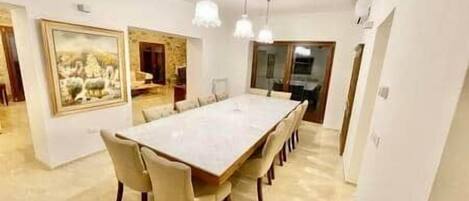 A dining room with a long table, chairs, pendant lights, and a large framed picture on the wall.