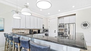 A modern kitchen with white cabinets, a large island with bar stools, stainless steel appliances, and pendant lighting. - Coastal Dream Home | Ocean Views & Rooftop Spa (Hilton Head Island)