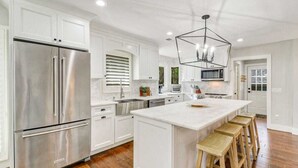 A modern kitchen with white cabinetry, a stainless steel refrigerator, a central island with stools, and a geometric pendant light.