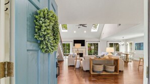 A spacious living room with a blue door, wooden flooring, a ceiling fan, and a dining area with a table and chairs.