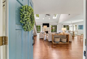 A spacious living room with a blue door, wooden flooring, a ceiling fan, and a dining area with a table and chairs.