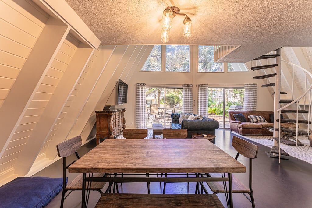 A dining area with a wooden table and chairs, a staircase, and a view of the outdoors.