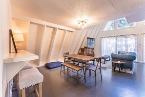A loft-style room with a dining table, benches, a sofa, and a TV.