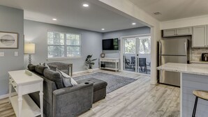 Un salón moderno con un sofá gris, una mesa de centro blanca y un televisor montado en la pared.