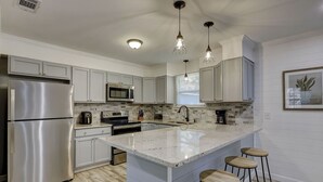 Una cocina moderna con electrodomésticos de acero inoxidable, una isla grande con taburetes e iluminación colgante.