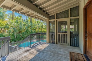 Una terraza de madera con piscina, rodeada de vegetación.