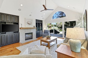 A spacious living room with a fireplace, a flat-screen TV, and a ceiling fan.