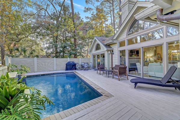 A swimming pool with a wooden deck, outdoor furniture, and a covered patio area.
