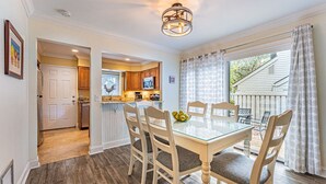 A dining area with a glass table and chairs, a kitchen in the background, and a view of the outside.