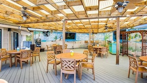 An outdoor patio area with wooden tables and chairs, ceiling fans, and a mural on the wall. - Coastal Getaway | Ocean Views & Resort Amenities (Hilton Head Island)