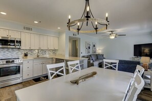 Une cuisine moderne avec des armoires blanches, un four encastré et un coin repas comprenant une table et des chaises blanches.