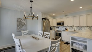 A modern kitchen with white cabinetry, a stainless steel refrigerator, and a dining area with a white table and chairs. - Coastal Getaway | Ocean Views & Resort Amenities (Hilton Head Island)