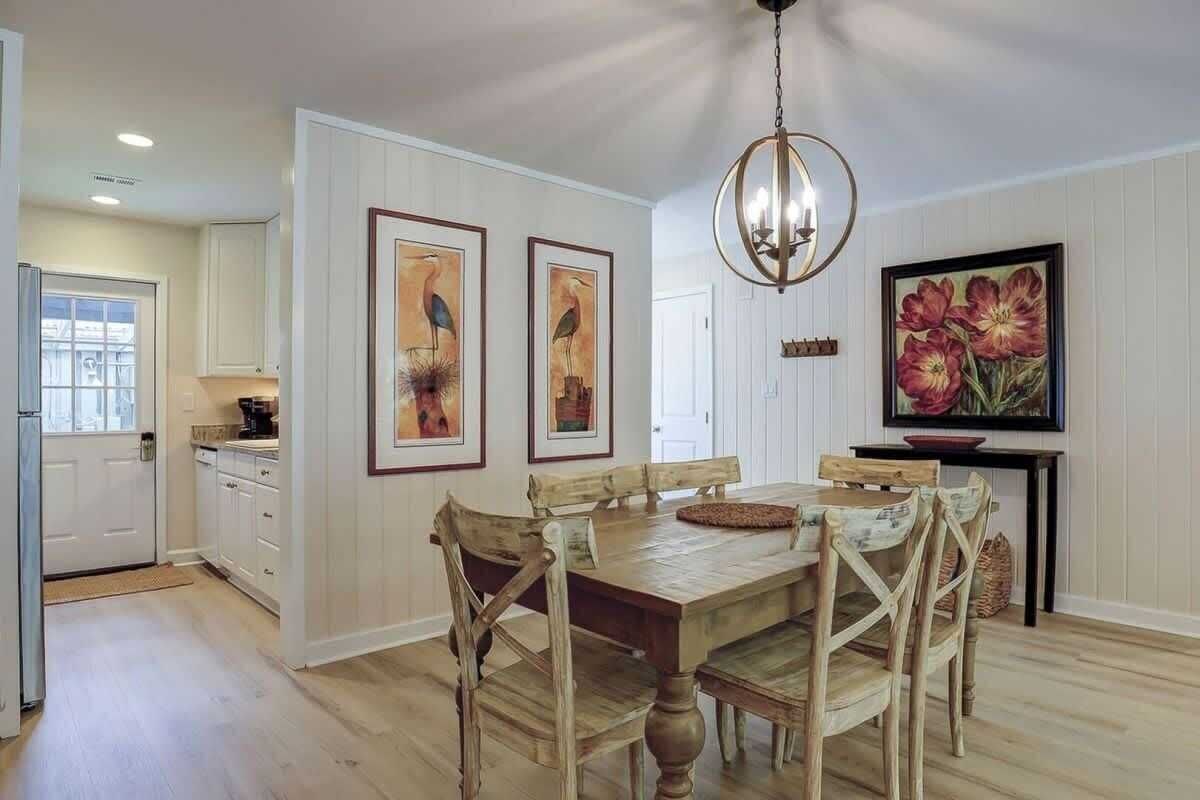 A dining area with a wooden table and chairs, a chandelier, and framed artwork on the walls.
