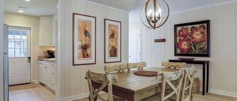 A dining area with a wooden table and chairs, a chandelier, and framed artwork on the walls.
