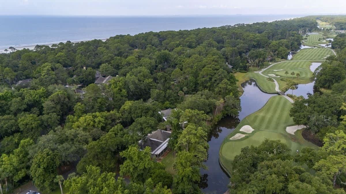 Luchtbeeld van een golfbaan met waterhindernissen, een clubhuis en dichte beboste gebieden.