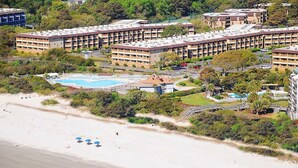 Ein mehrstöckiges Hotel mit Pool, Zugang zum Strand und einer angelegten Grünfläche.