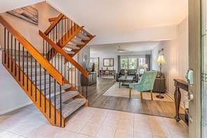 A spacious living area with a wooden staircase, a fireplace, and a view of the outdoors.