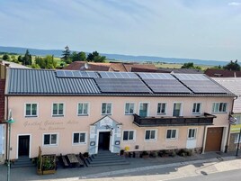 A building with solar panels on the roof, a sign reading "Gasthof Goldener Adler," and a view of the countryside.