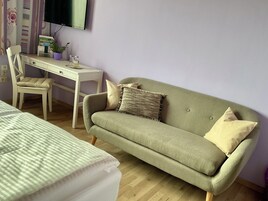 Una habitación con un sofá verde, un escritorio blanco, una silla y una cama con ropa de cama a rayas.